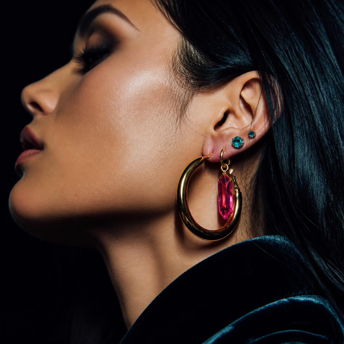 Crystal chandelier earrings, chunky gold hoops, hot pink resin hoops, turquoise studs and orange beaded tassel earrings arranged on black velvet